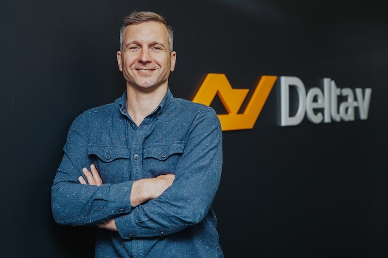 CEO of Delta-v, Alex Gasson, standing with arms folded, against Delta-v logo as backdrop.